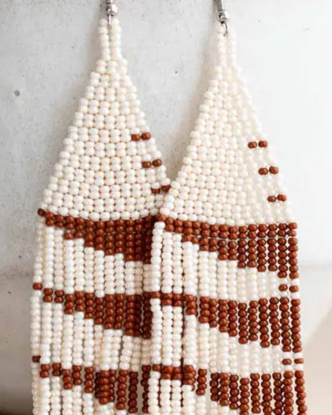 Pair of beaded earrings with white and brown beads on a light gray background