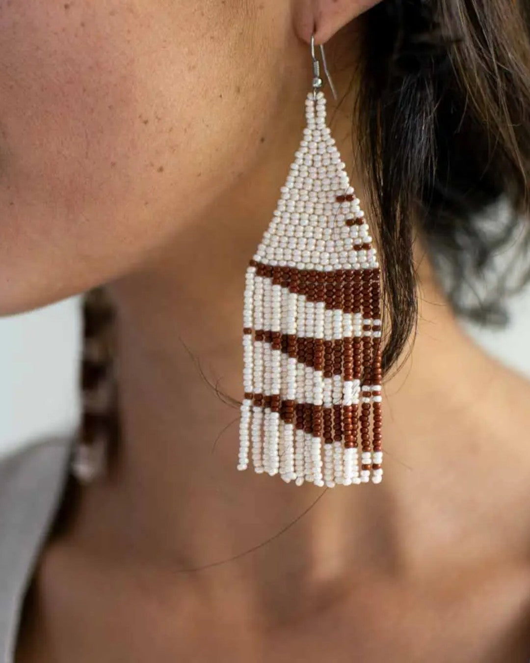 Beaded earrings with white and brown pattern worn by a person