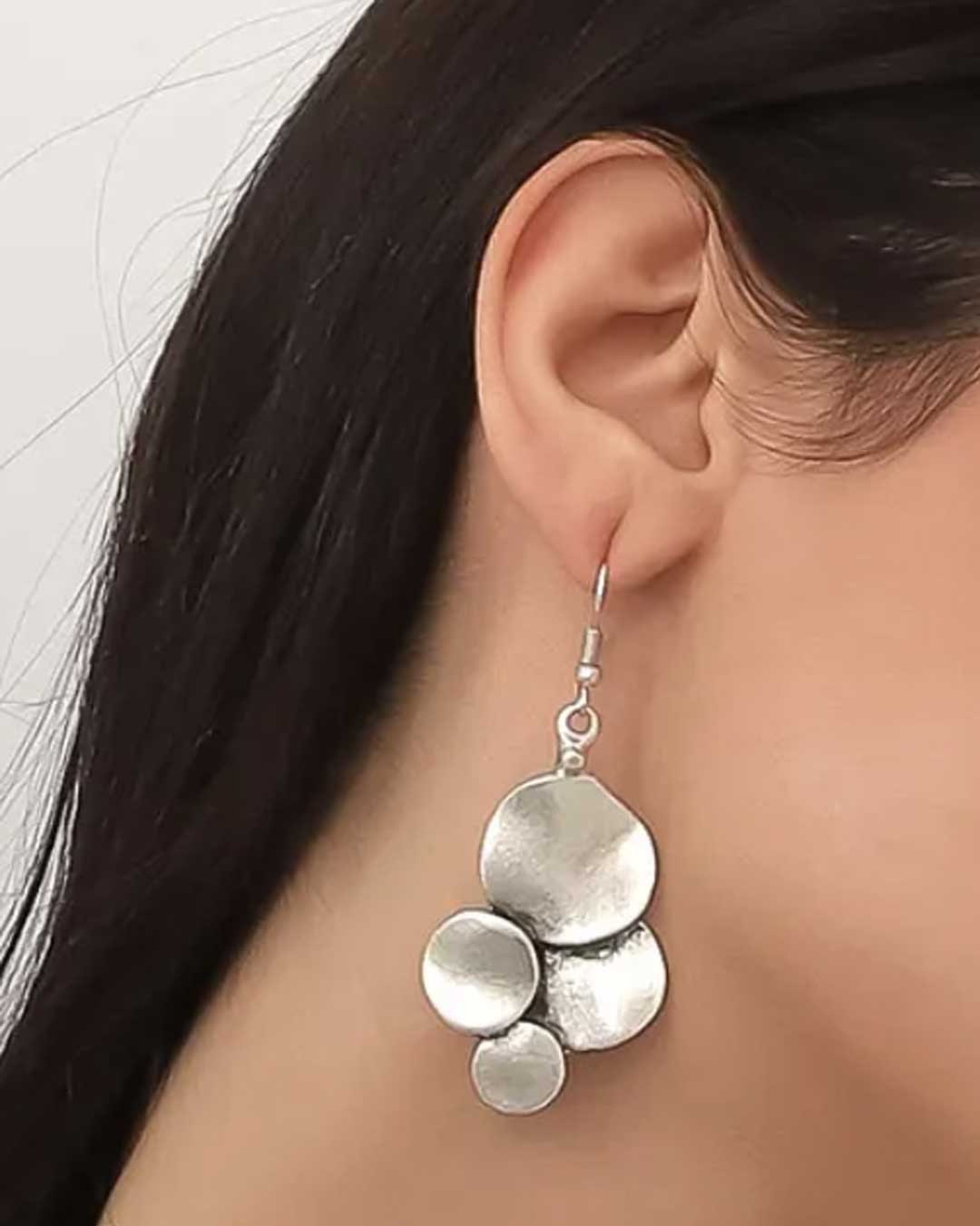 Silver earrings worn by a person with dark hair against a neutral background