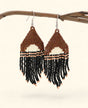 Pair of beaded earrings with brown, white, and black colors hanging on a branch.