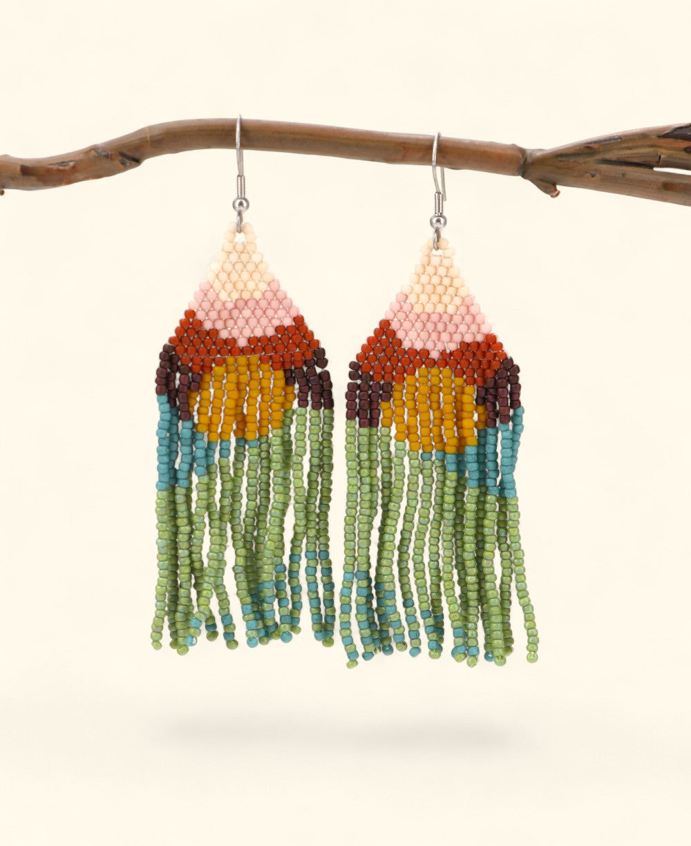 Colorful beaded earrings hanging from a branch on a light background