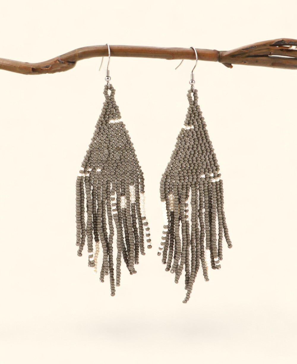 Beaded earrings hanging from a branch on a light background