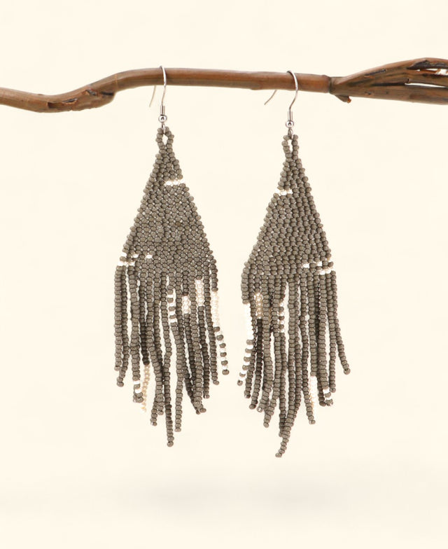 Beaded earrings hanging from a branch on a light background