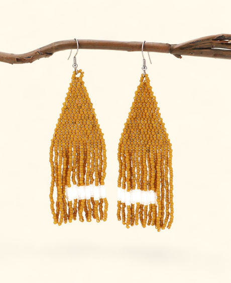 Pair of yellow beaded earrings hanging from a branch on a beige background