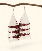 White beaded earrings with red accents hanging on a branch against a white background