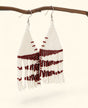 White beaded earrings with red accents hanging on a branch against a white background