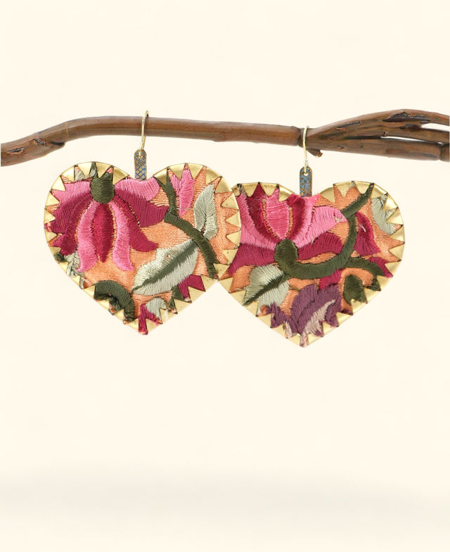 Heart-shaped embroidered earrings on a branch against a white background
