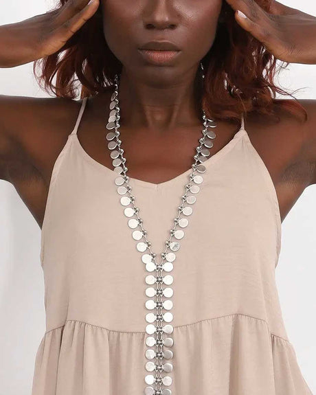 Woman wearing a beige dress with a long silver necklace against a white background