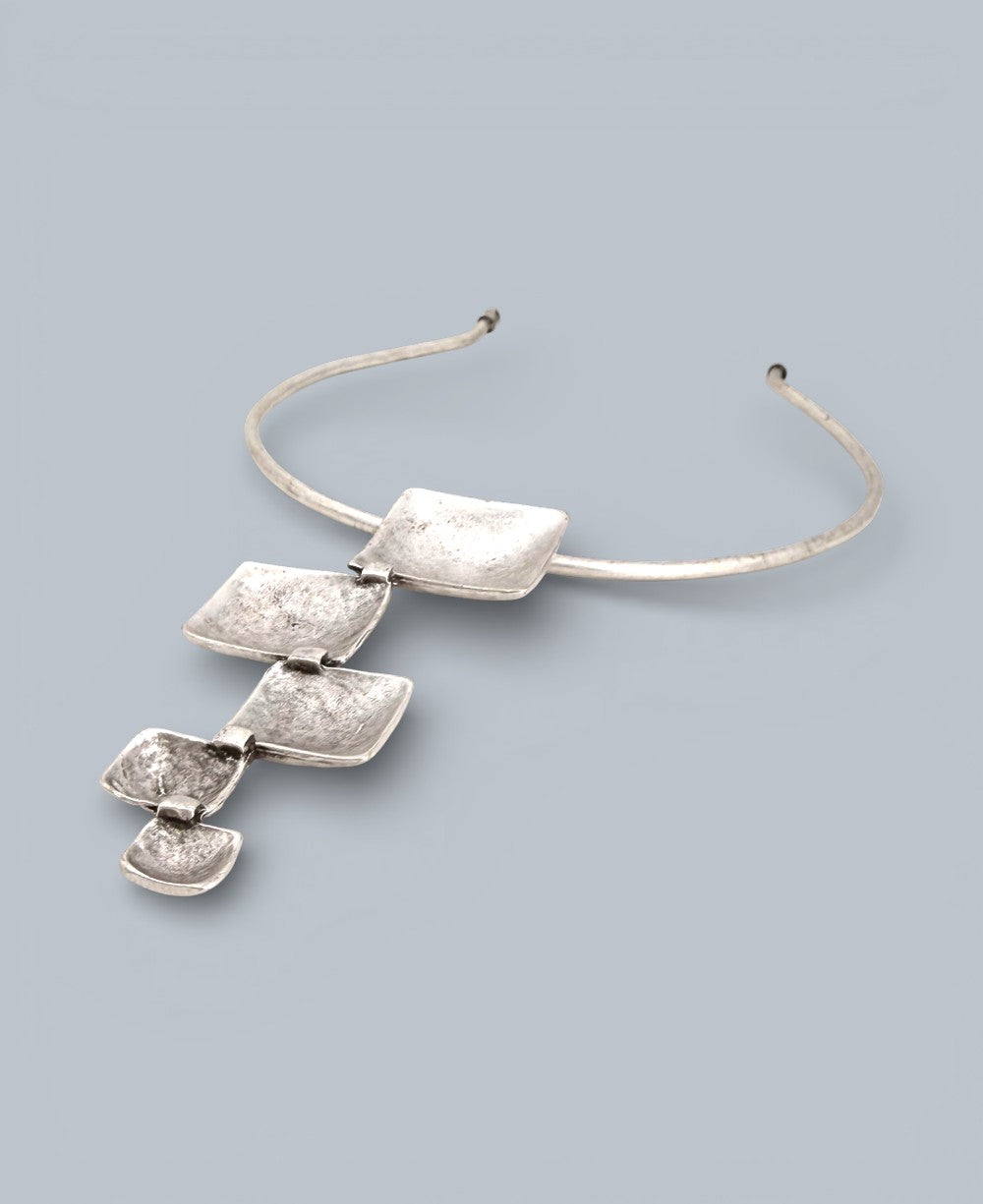 Silver necklace with three pendant elements on a light gray background