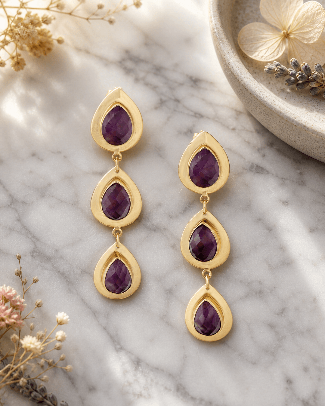 Amethyst teardrop earrings with faceted purple gemstones on a white marble background