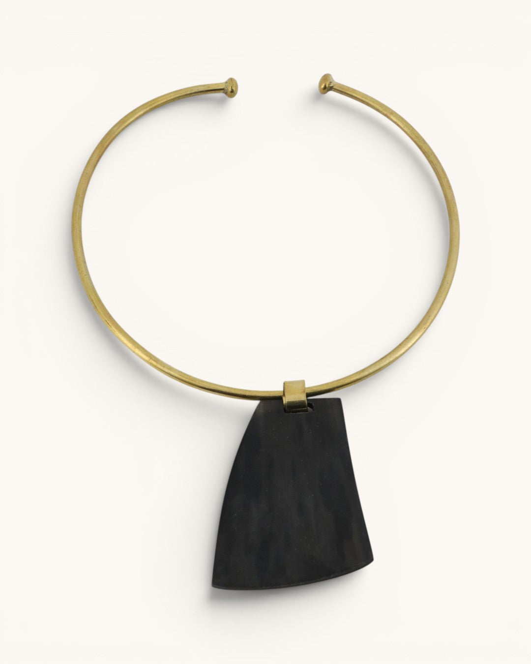 Ankole horn pendant brass choker necklace flat lay, dark trapezoidal horn piece on open brass collar, white background
