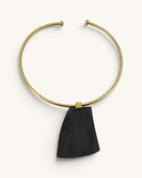 Ankole horn pendant brass choker necklace flat lay, dark trapezoidal horn piece on open brass collar, white background
