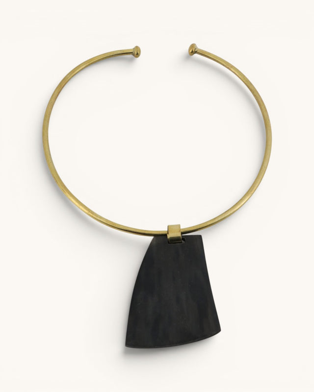 Ankole horn pendant brass choker necklace flat lay, dark trapezoidal horn piece on open brass collar, white background