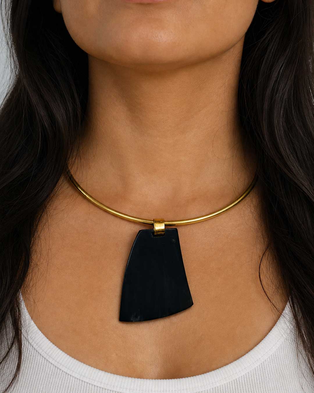 Ankole horn pendant brass choker necklace worn on model, large dark horn pendant centered on gold-tone rigid collar at neckline