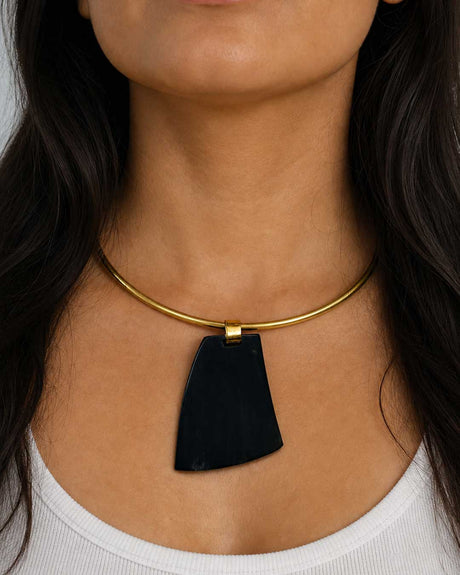Ankole horn pendant brass choker necklace worn on model, large dark horn pendant centered on gold-tone rigid collar at neckline