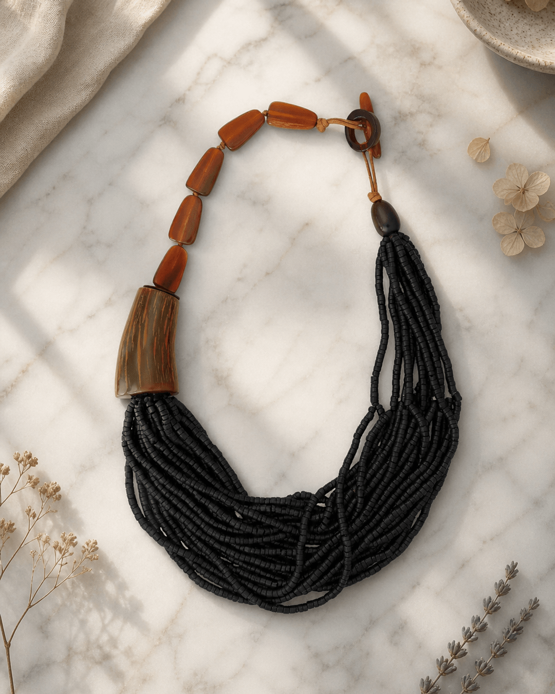 Black asymmetric necklace with horn pendants and coconut beads on white marble surface