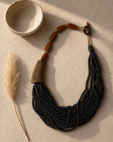 Black asymmetric necklace with horn and coconut beads displayed against a plaster surface with dramatic editorial shadow
