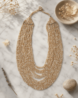 Beige and gold-tone multi-strand glass beaded necklace displayed on white marble surface