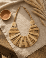 Beige statement bib necklace with layered tones displayed on linen fabric beside a journal