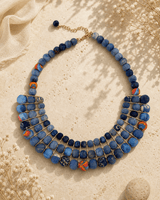Blue textile-wrapped bead layered necklace displayed on travertine surface