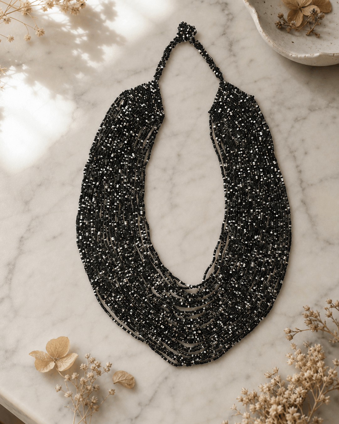 Black and grey multi-strand glass beaded necklace displayed on white marble surface