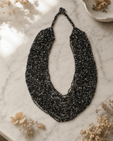 Black and grey multi-strand glass beaded necklace displayed on white marble surface