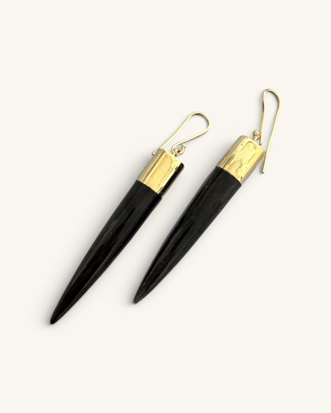 Kami black horn brass spike drop earrings pair on white background, diagonal angle revealing hand-carved texture along spike length