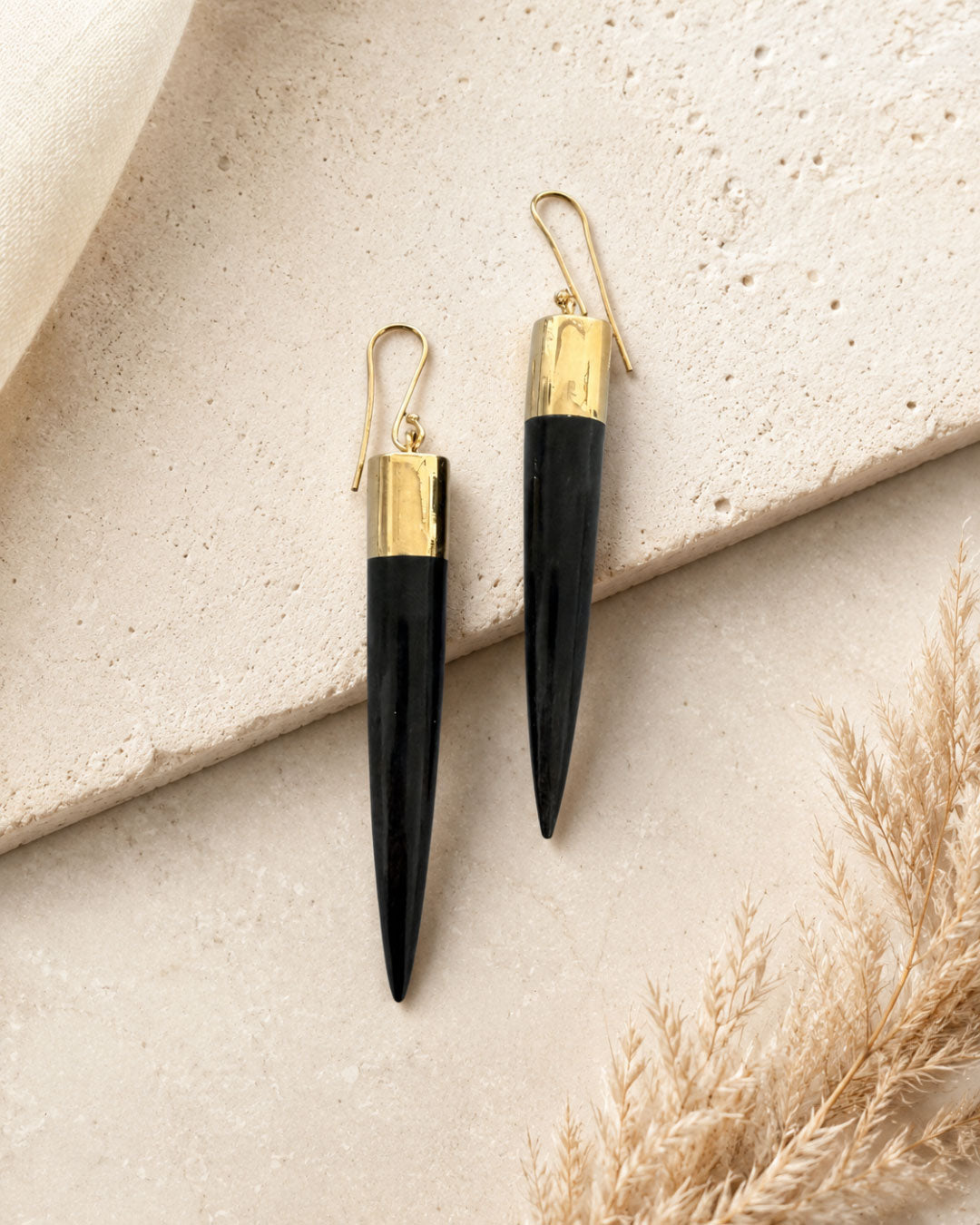 Kami black horn brass spike drop earrings laid flat on stone surface with dried pampas grass, styled flat-lay pair view
