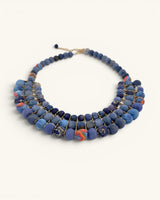 Blue textile-wrapped bead layered necklace at an angle, showing mixed-pattern accent beads and gold wire bar detail