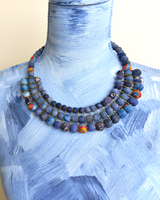 Blue textile-wrapped bead layered necklace displayed on a blue mannequin bust, showing full bib silhouette and clasp