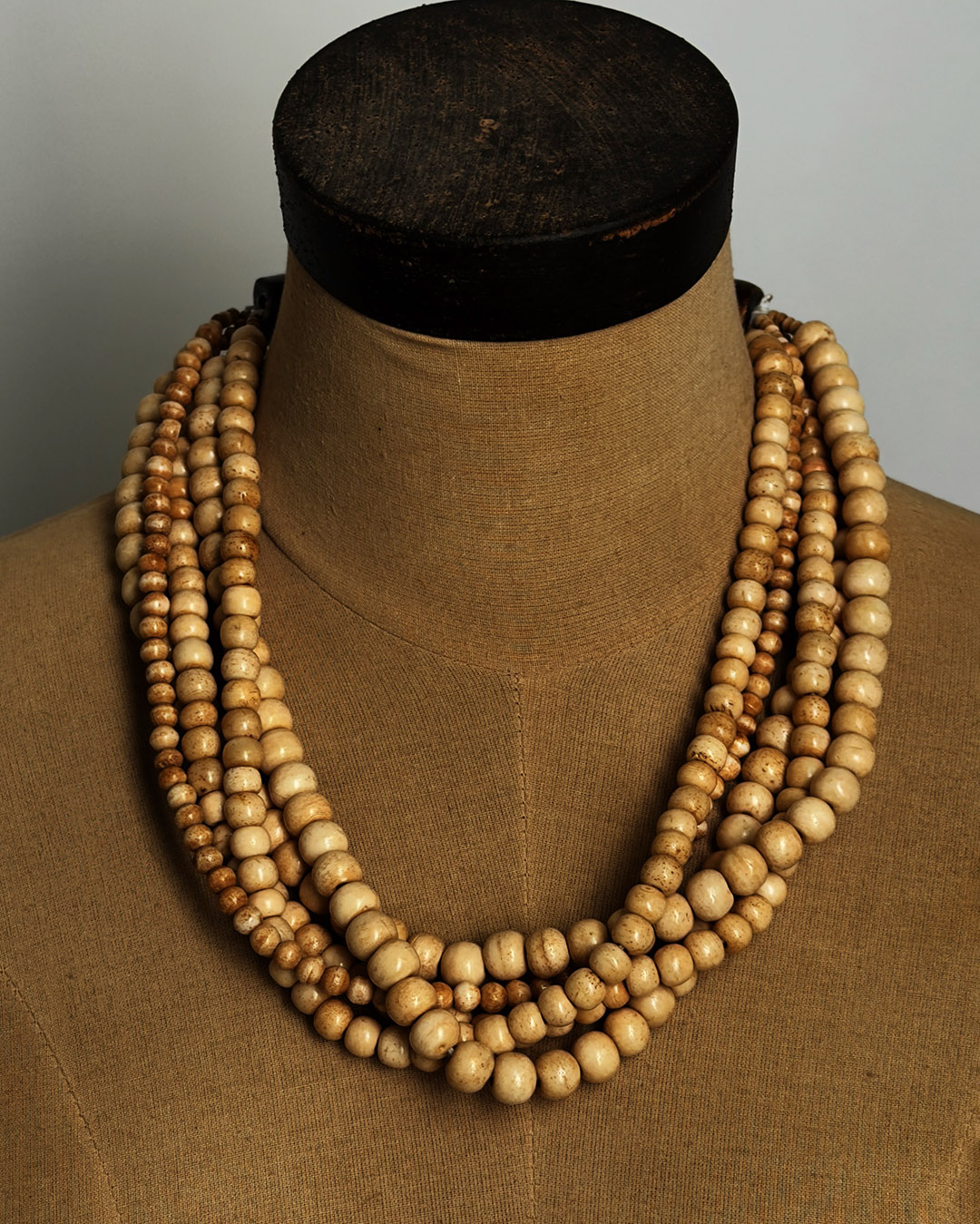 Five-strand Indian bone bead necklace draped on a burlap dress form, showing layered strand arrangement from front
