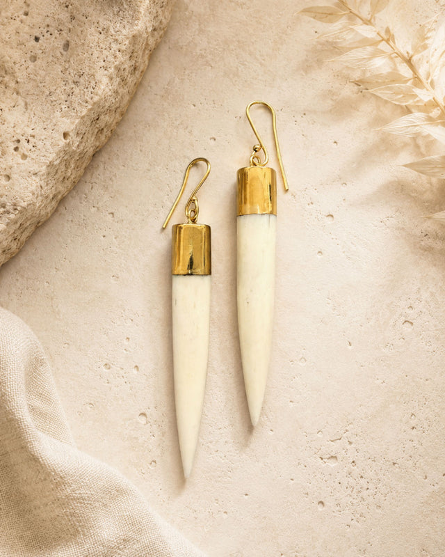 Kenyan hand-carved bone and brass spike dangle earrings laid flat on a stone surface with dried botanicals, styled view