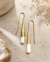 Tosha bone and brass threader drop earrings laid flat on stone surface with dried flowers and crystal props