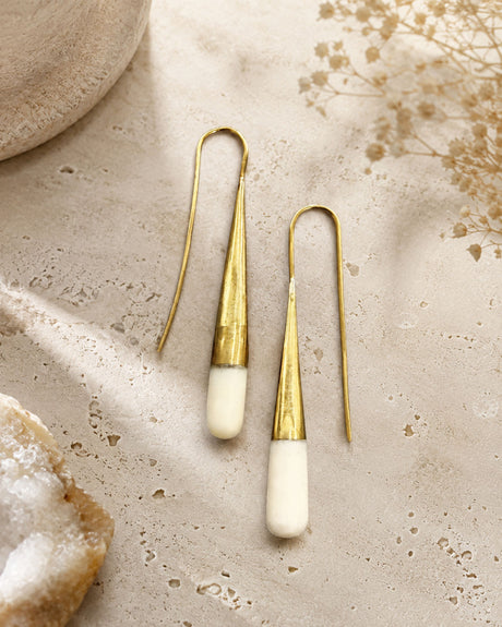 Tosha bone and brass threader drop earrings laid flat on stone surface with dried flowers and crystal props