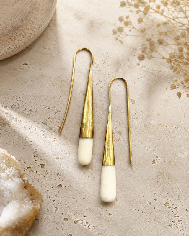 Tosha bone and brass threader drop earrings laid flat on stone surface with dried flowers and crystal props