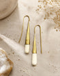Tosha bone and brass threader drop earrings laid flat on stone surface with dried flowers and crystal props