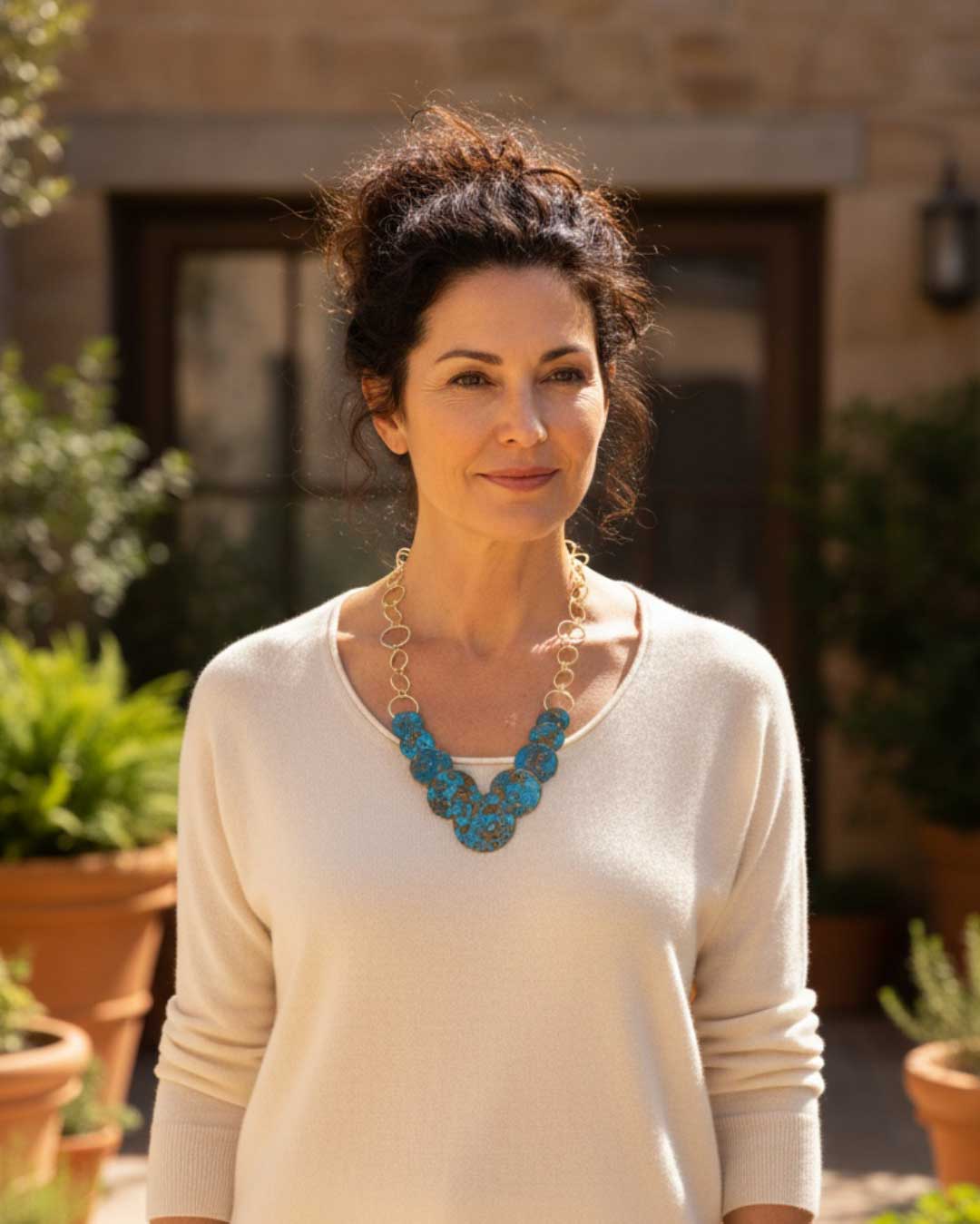 Hand-forged brass necklace with blue patina discs laid out in overhead flat-lay view on a neutral background