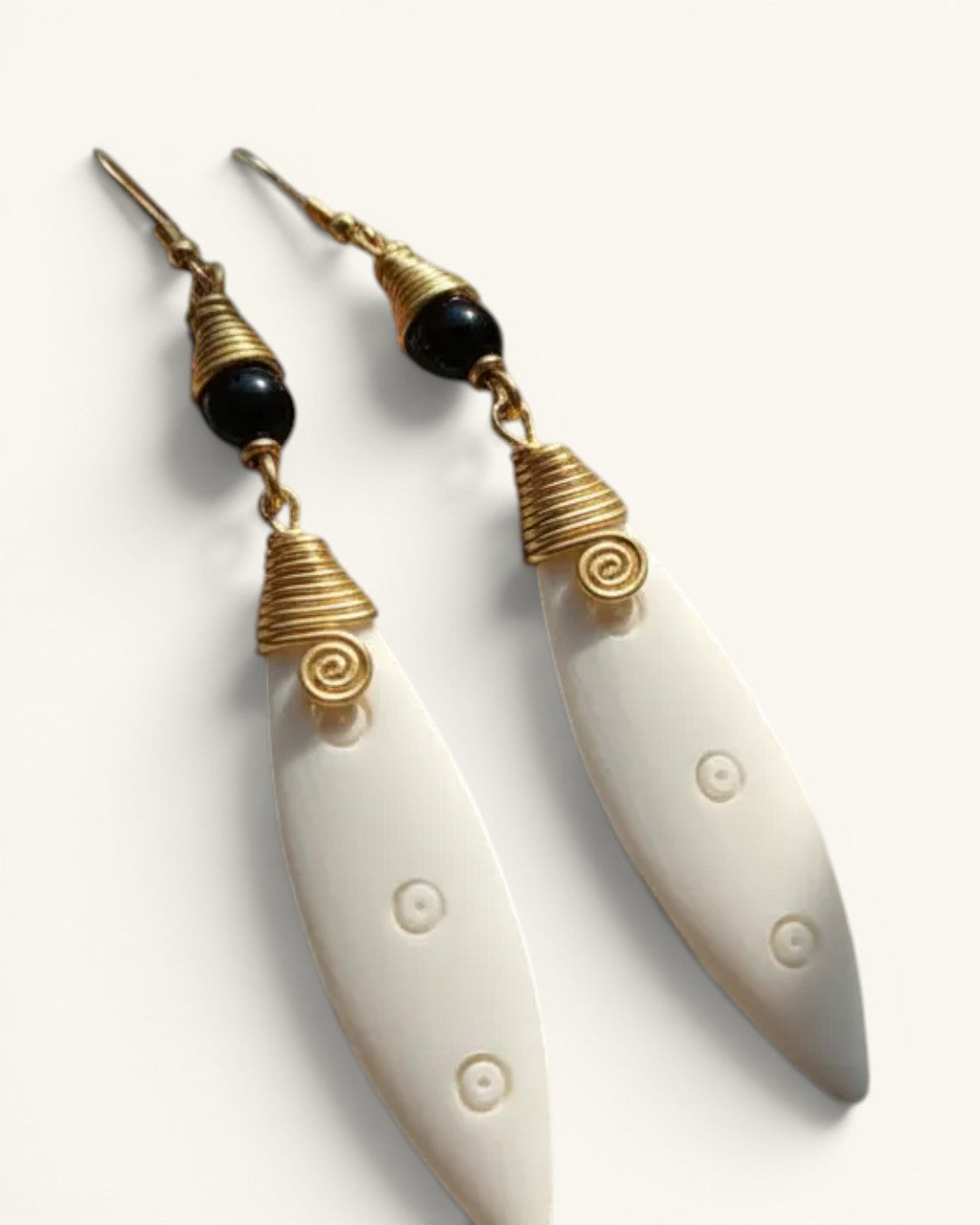 Close-up detail of both Kenyan artisan earrings showing brass coil caps, black beads, spiral motif, and carved bone pendants