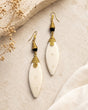 Kenyan hand-coiled brass and carved bone drop earrings styled on stone surface with dried flowers and white linen fabric