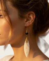 Brass-coiled carved bone drop earring worn by a model with auburn hair, side profile showing earring length against neck
