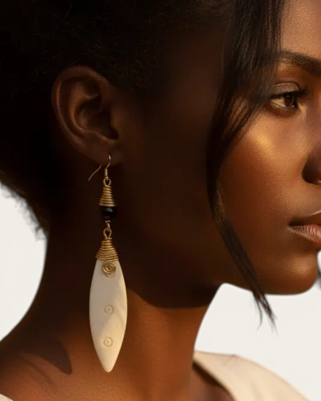 Carved bone drop earring with coiled brass cap and black bead worn by a model, close side profile showing full drop length
