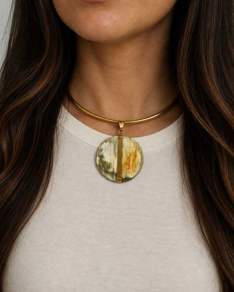 Brass collar choker with Ankole horn disc pendant worn on a model at the neckline over a white top, front view