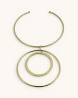 Hand-forged brass collar necklace with two concentric ring pendants, flat lay on white background