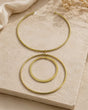 Brass collar necklace with double ring pendants laid flat on a stone surface with linen and dried florals
