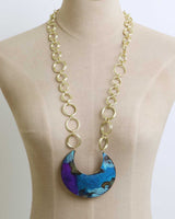 Hand-patinated brass crescent pendant necklace on a beige dress form showing pendant length and scale against the body