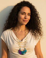 Hand-patinated brass crescent pendant necklace worn by a model in a white top photographed outdoors in warm golden light