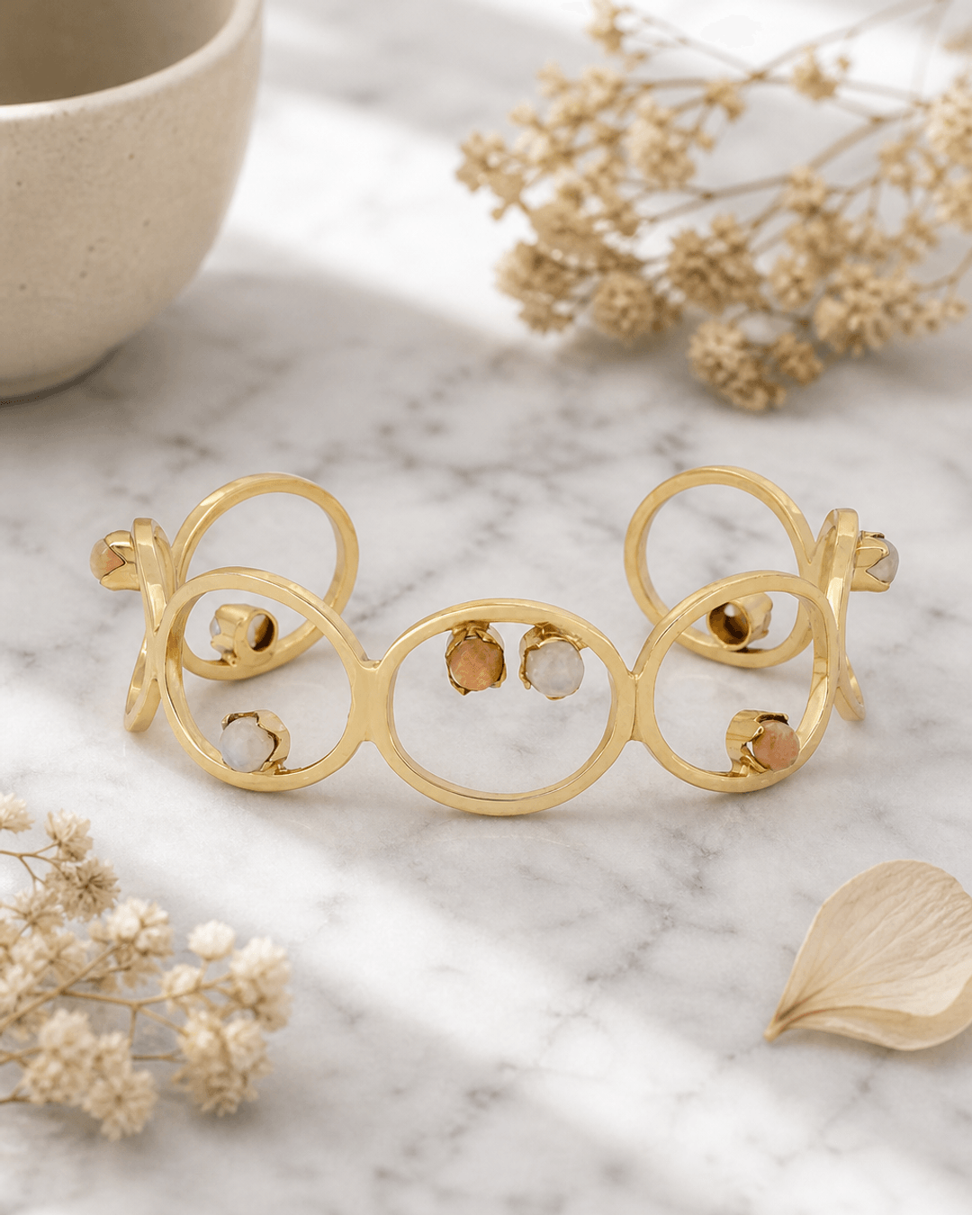 Brass cuff bracelet with moonstone and peach moonstone gemstones displayed on white marble surface