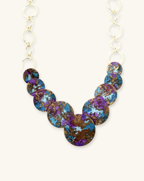Close-up detail of hand-forged brass disc necklace showing hammer texture and purple blue patina finish