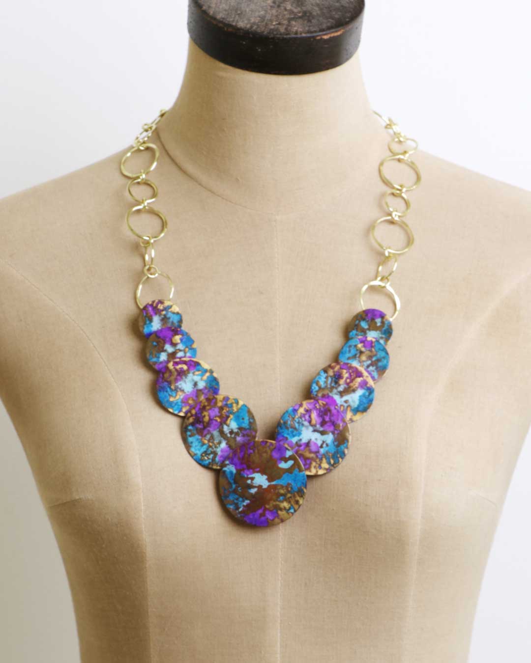 Front view of Indian hand-forged brass disc necklace with purple and blue patina against neutral background