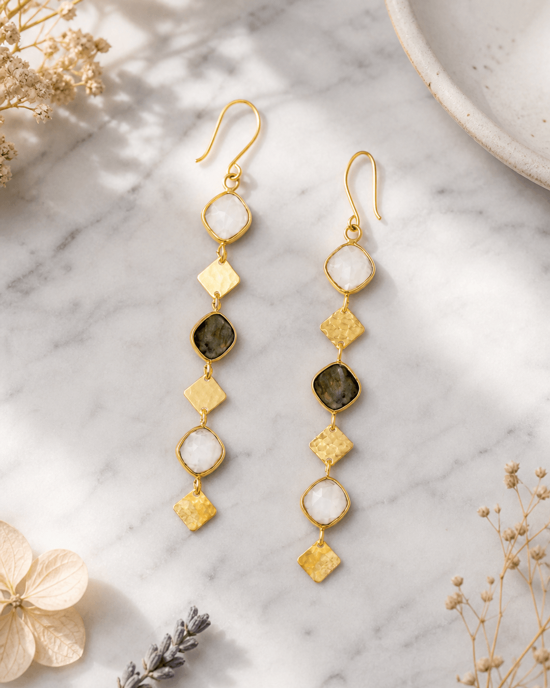 Brass drop earrings featuring labradorite and moonstone gemstones displayed on white marble surface